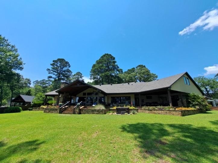 Spacious Ranch-Style House with Stone Steps and Lush Green Lawn Surrounded by Tall Trees Under a Clear Blue Sky