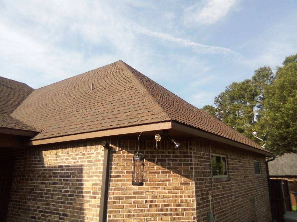 Brick House Corner with Brown Shingle Roof and Outdoor Security Lights Under Clear Blue Sky