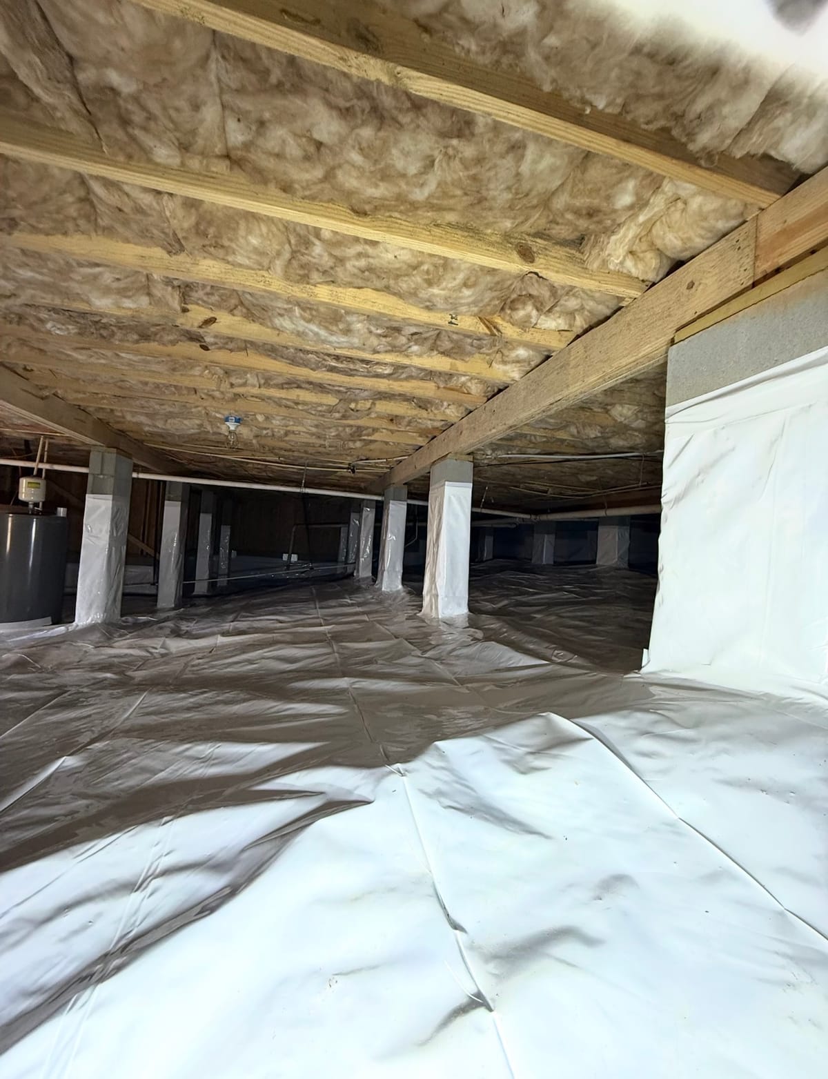 Crawl Space with Insulation and Vapor Barrier Lining Featuring Exposed Wooden Beams and Wrapped Support Columns