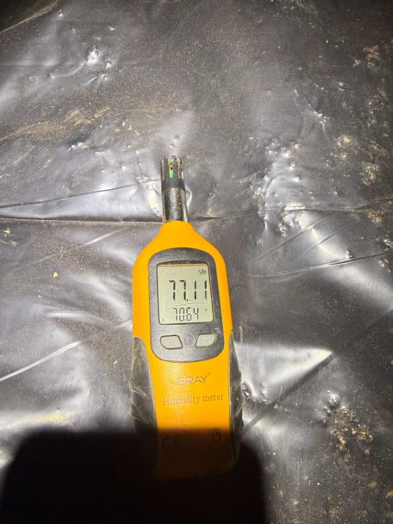 Digital Humidity Meter Displaying HIGH RELATIVY HUMIDITY 77.1% on Black Textured Surface with Visible Dirt and Scratches
