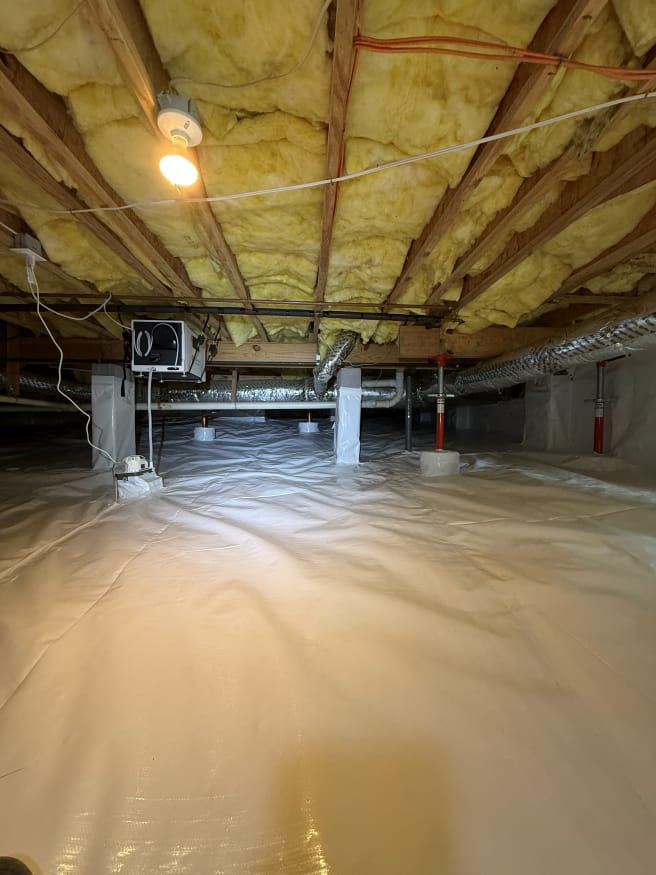 Illuminated Crawl Space with Insulation and Vapor Barrier Featuring Exposed Wooden Beams and Network of Metal Ducts and Wiring
