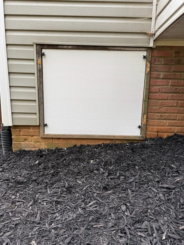 White Crawl Space Access Door on Brick and Vinyl House Exterior with Black Mulch Ground Covering