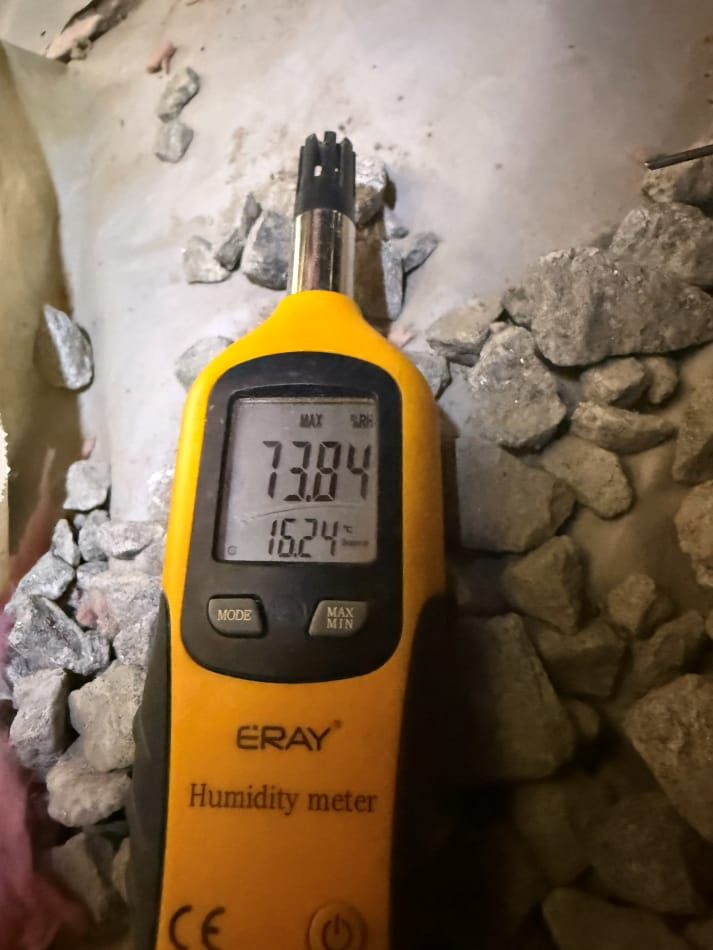 Yellow Handheld Humidity Meter Displaying Readings of 73.84% Humidity and 16.24°C Temperature on Gravel Surface