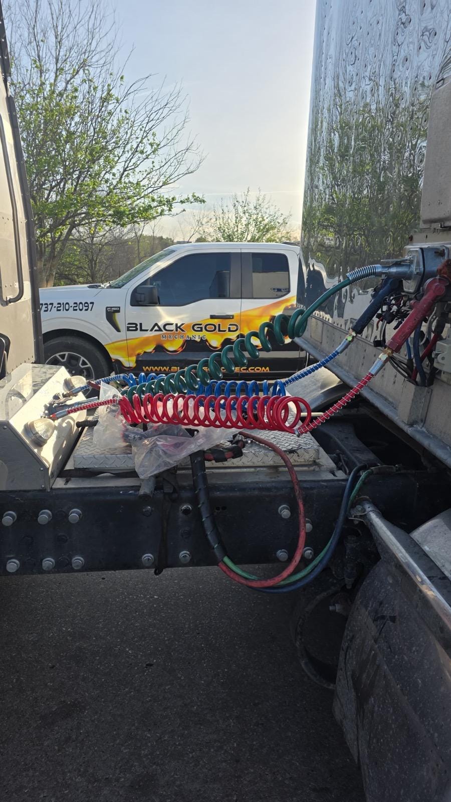 Coiled Air and Electrical Lines on Semi-Truck Hitch with Company Service Vehicle in Background on Sunny Day
