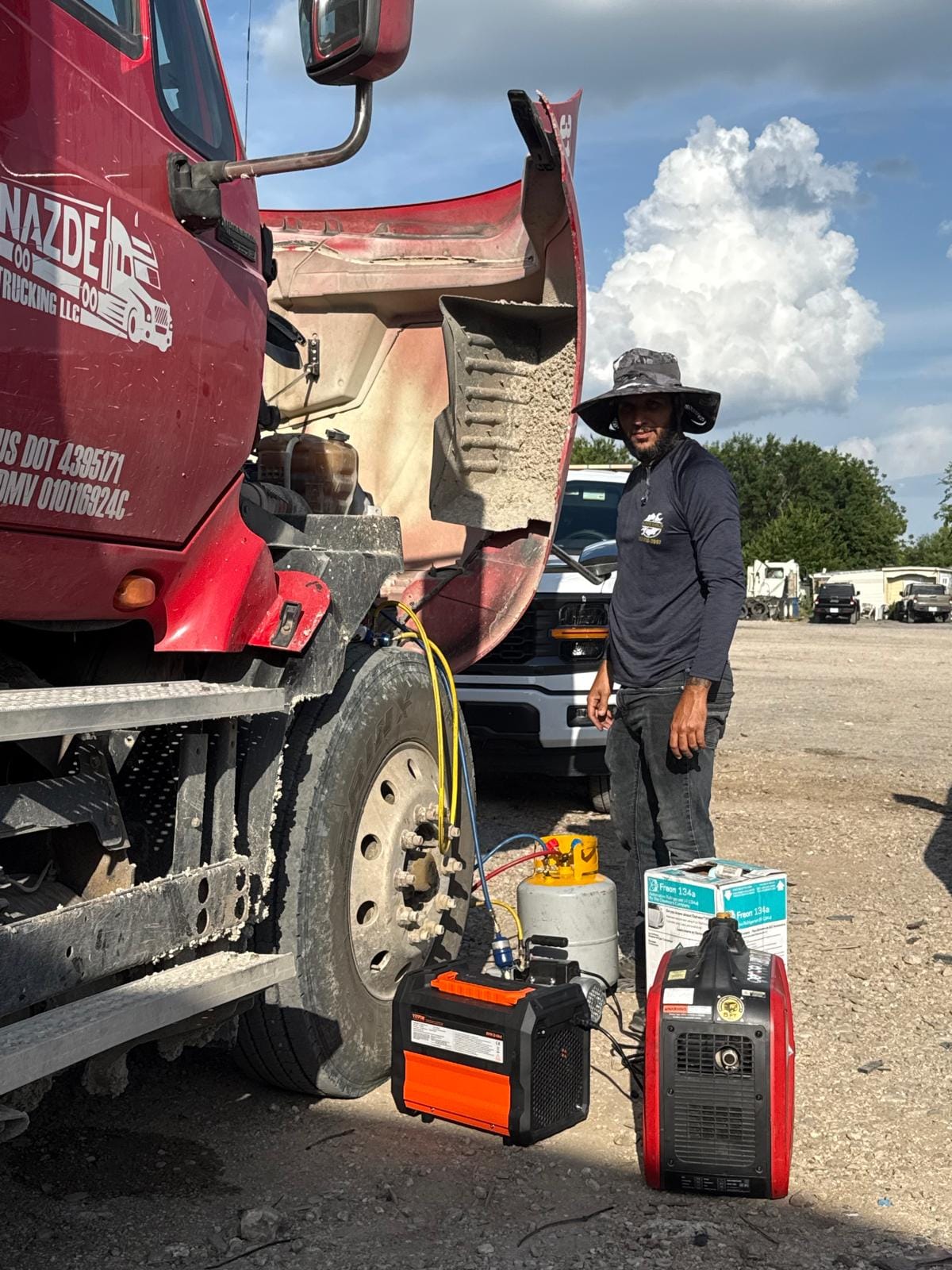 Mechanic Performing Maintenance on a Red Truck with Hood Raised, Surrounded by Tools and Equipment in a Sunny Outdoor Setting