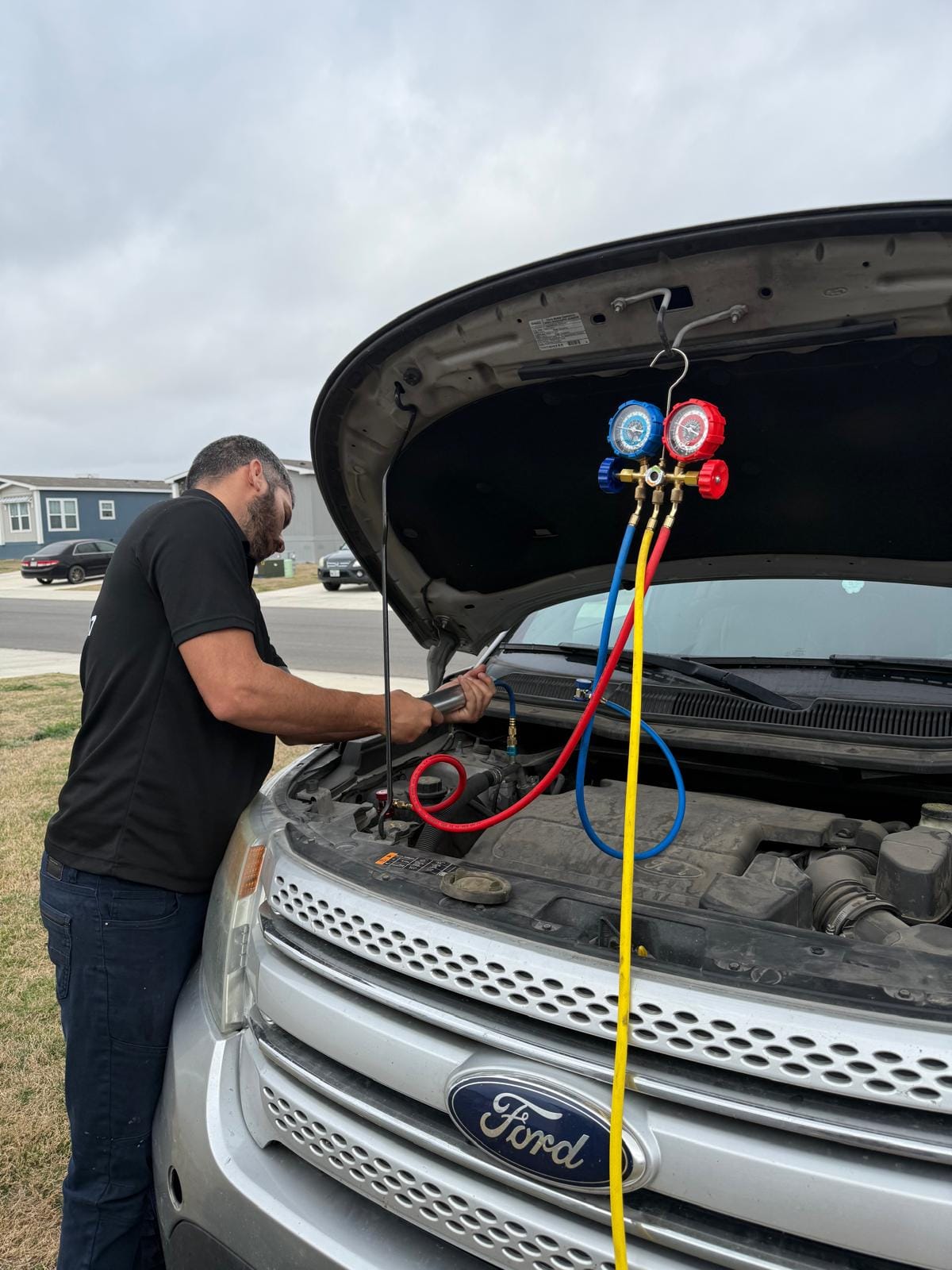 Mechanic Performing Air Conditioning System Maintenance on a Ford Vehicle with Manifold Gauge Set Under Cloudy Sky
