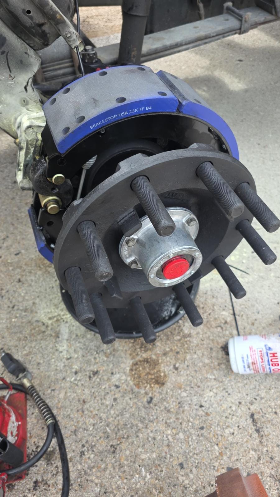 Close-Up of Vehicle Brake Assembly with Blue Brake Pads and Exposed Lug Bolts on Concrete Surface with Tools Nearby