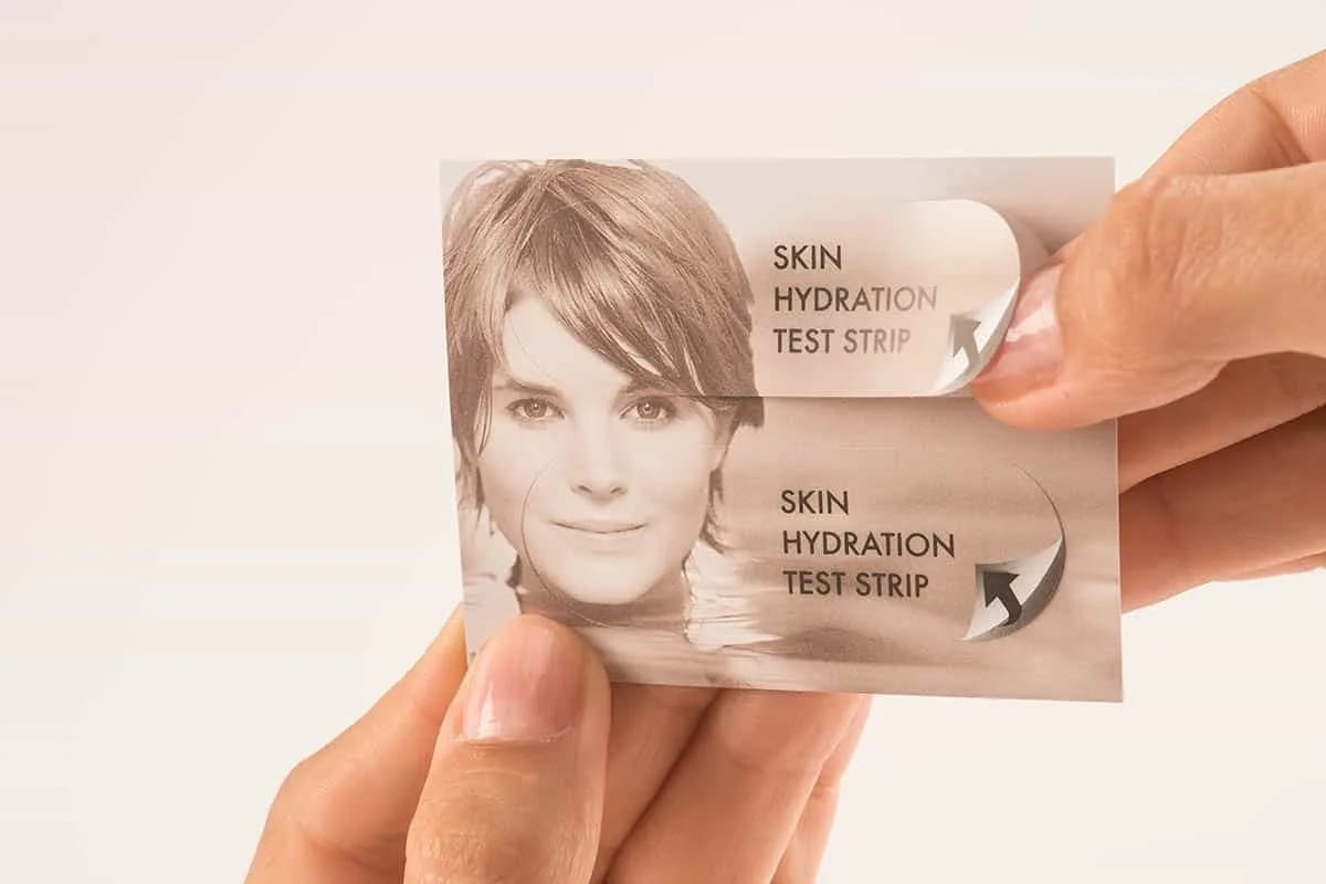 Close-Up of Hands Holding Skin Hydration Test Strip Card Featuring Woman’s Face and Text with Peeling Section