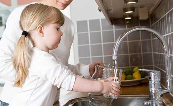 Young Child Learning to Fill Glass with Water at Kitchen Sink with Adult Supervision