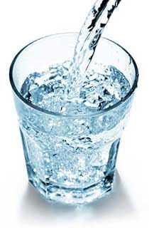 Clear Water Being Poured Into a Transparent Glass with Ice Cubes on a White Background