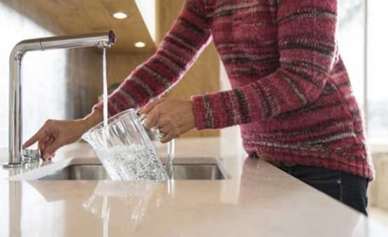 Person Filling Glass Pitcher with Water from Modern Kitchen Faucet