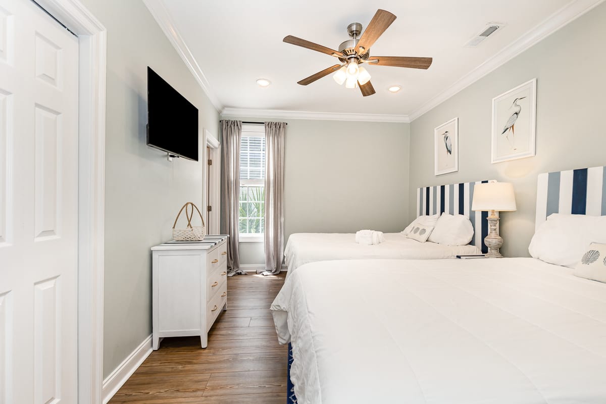 Cozy Modern Bedroom with Twin Beds, Striped Headboards, and Elegant Decor Featuring Wooden Floor, Ceiling Fan, Wall-Mounted TV, and Soft Natural Lighting Through Window Drapes