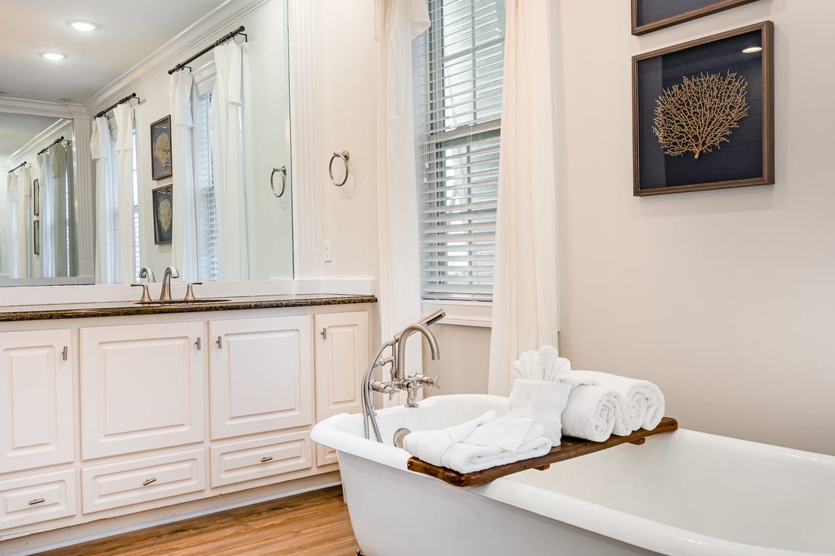Elegant Bathroom Interior with Clawfoot Tub, Wooden Vanity, Large Mirror, and Seashell-Themed Wall Art Featuring Rolled Towels and Natural Light from Shuttered Window