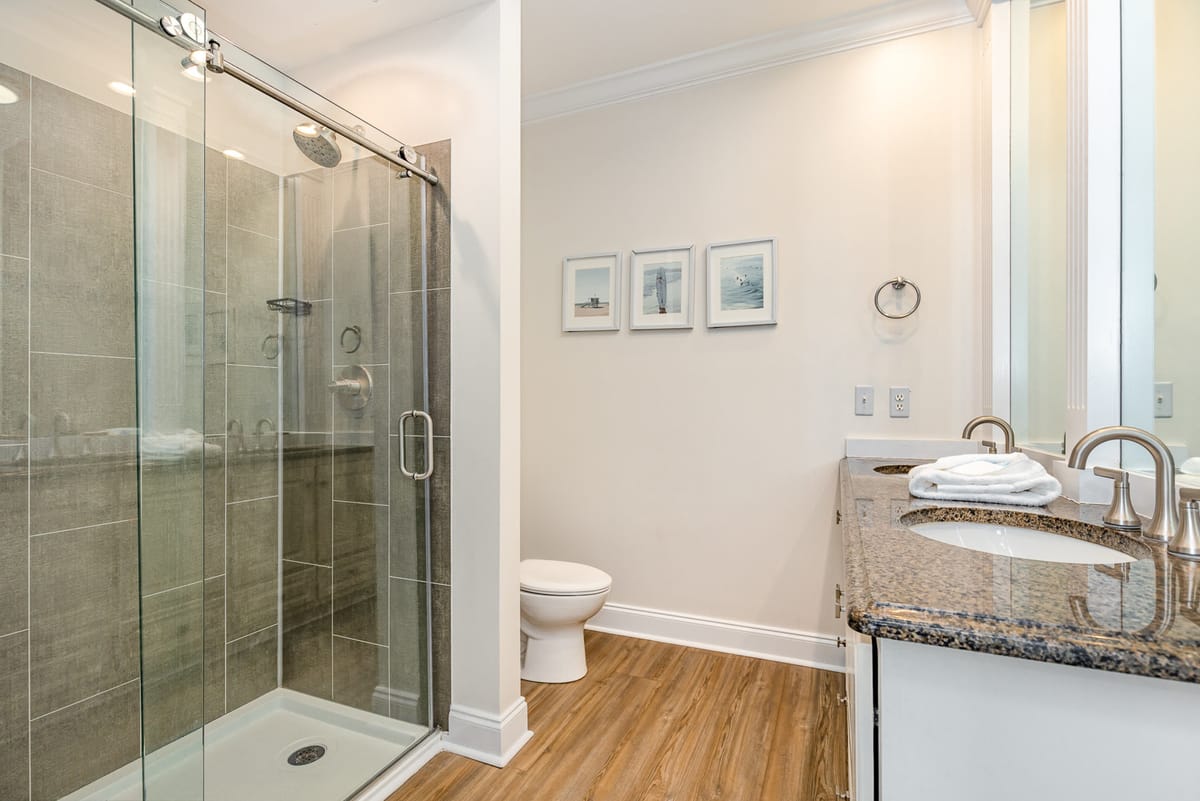 Modern Bathroom with Glass-Enclosed Shower, Granite Double Vanity, and Wooden Flooring Featuring Minimalist Decor and Framed Wall Art