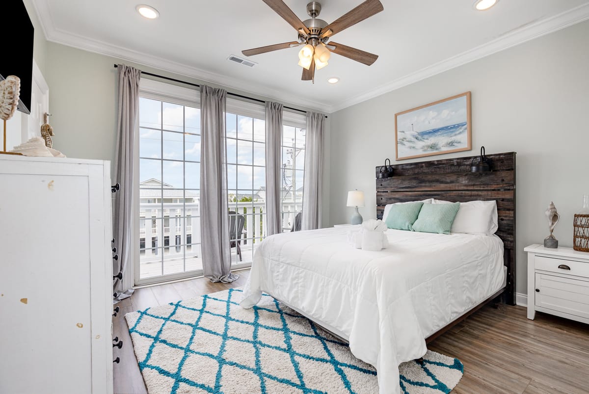 Bright Coastal-Themed Bedroom with Large Windows, Wooden Headboard, and Blue-Patterned Rug