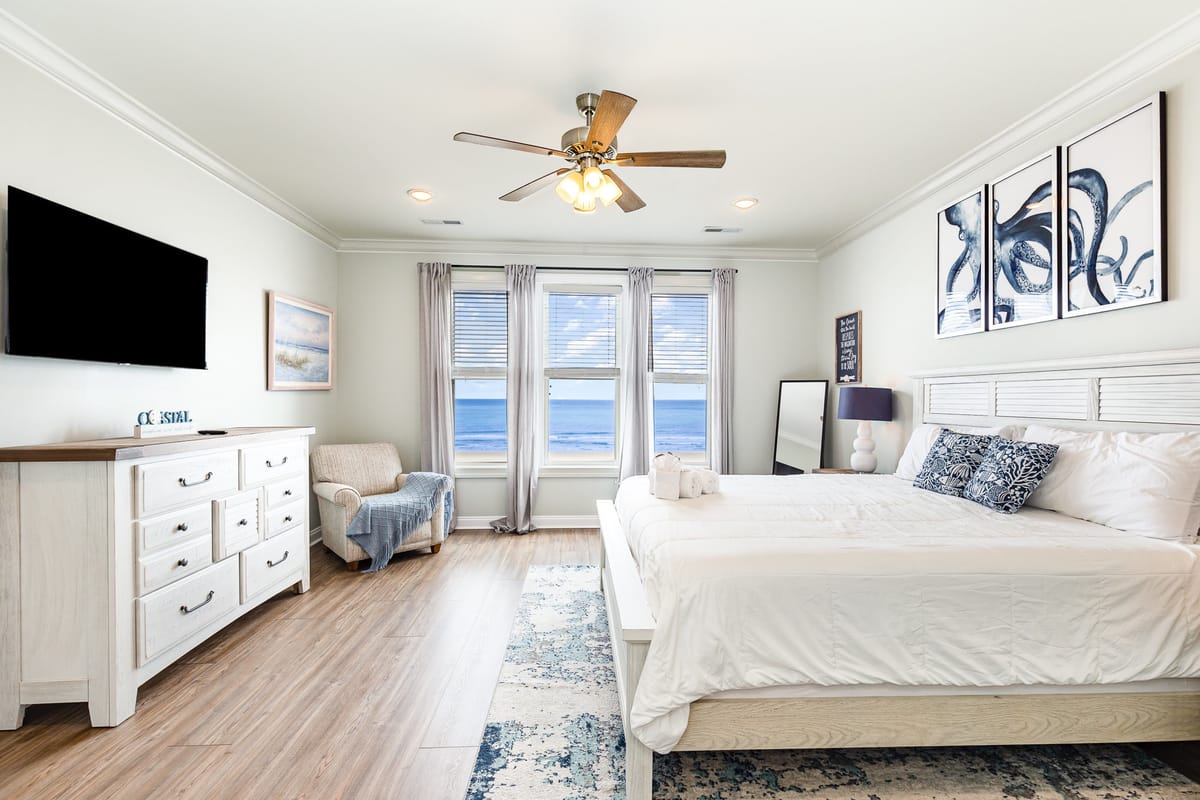 Coastal-Themed Bedroom with Ocean View, White Furniture, and Nautical Decor Featuring Ceiling Fan and Large Windows Overlooking the Sea