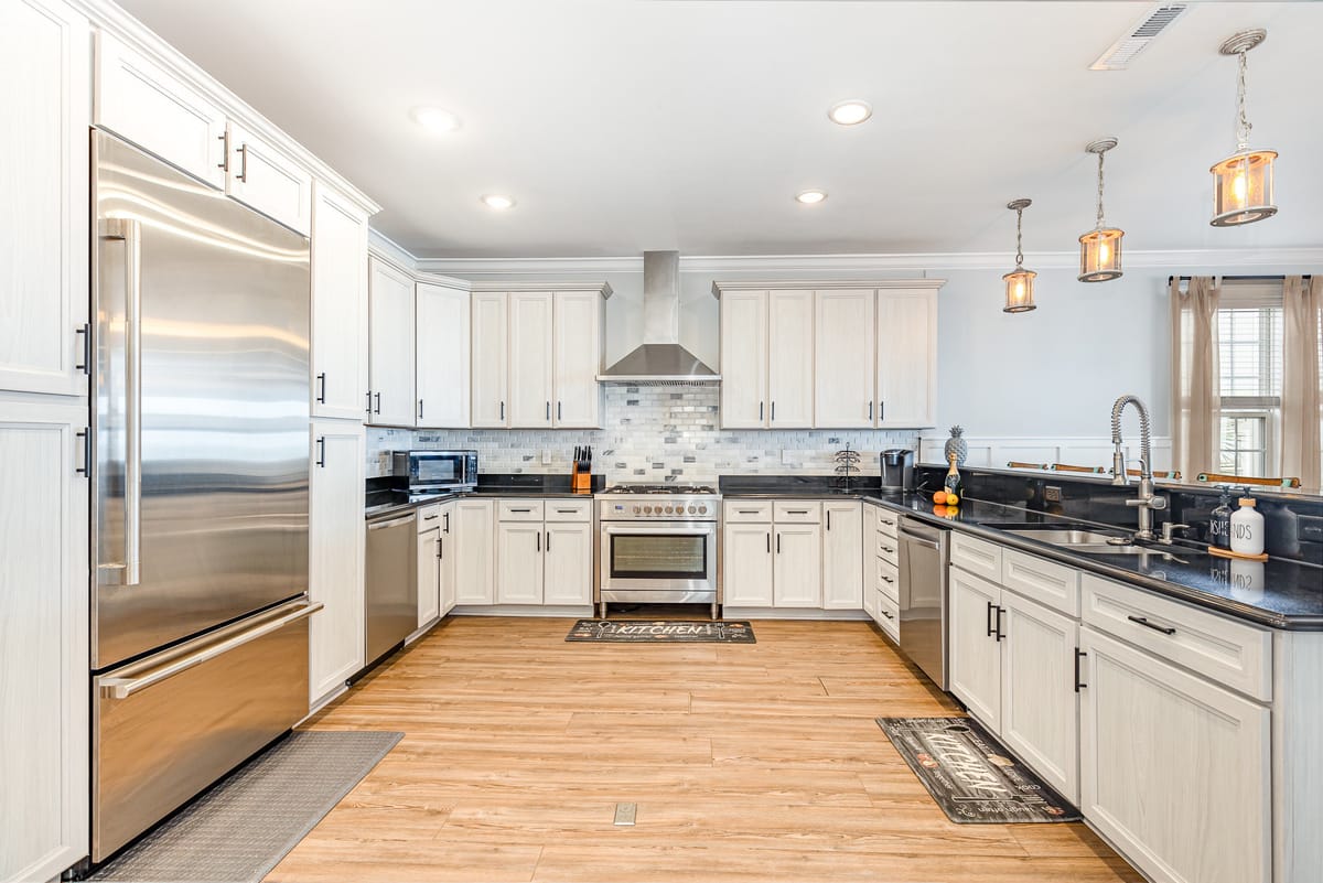 Spacious Modern Kitchen with Stainless Steel Appliances, White Cabinets, Dark Countertops, and Rustic Hanging Pendant Lights