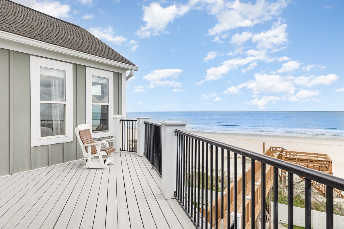Coastal Beach House Balcony Overlooking Serene Ocean View with Wooden Decking and White Adirondack Chair Under Partly Cloudy Blue Sky