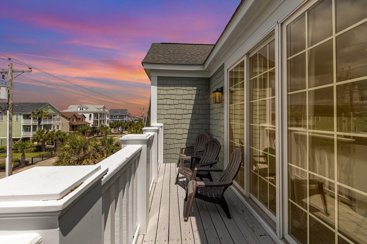 Charming Beachfront Balcony with Adirondack Chairs Overlooking Coastal Neighborhood at Sunset with Vibrant Purple and Orange Sky