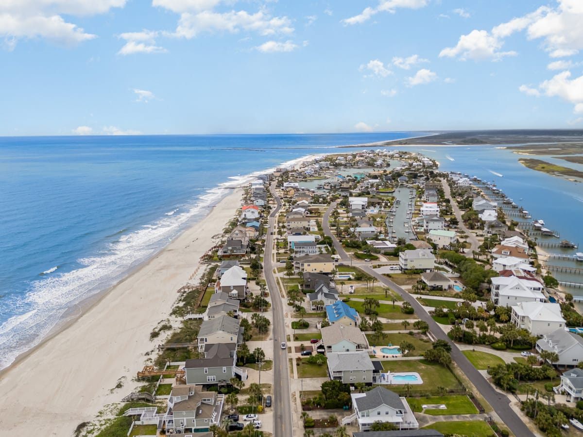 Coastal Aerial View of Expansive Sandy Beach and Oceanfront Houses with Clear Blue Skies and Gentle Waves Alongside a Serene Waterfront Residential Community