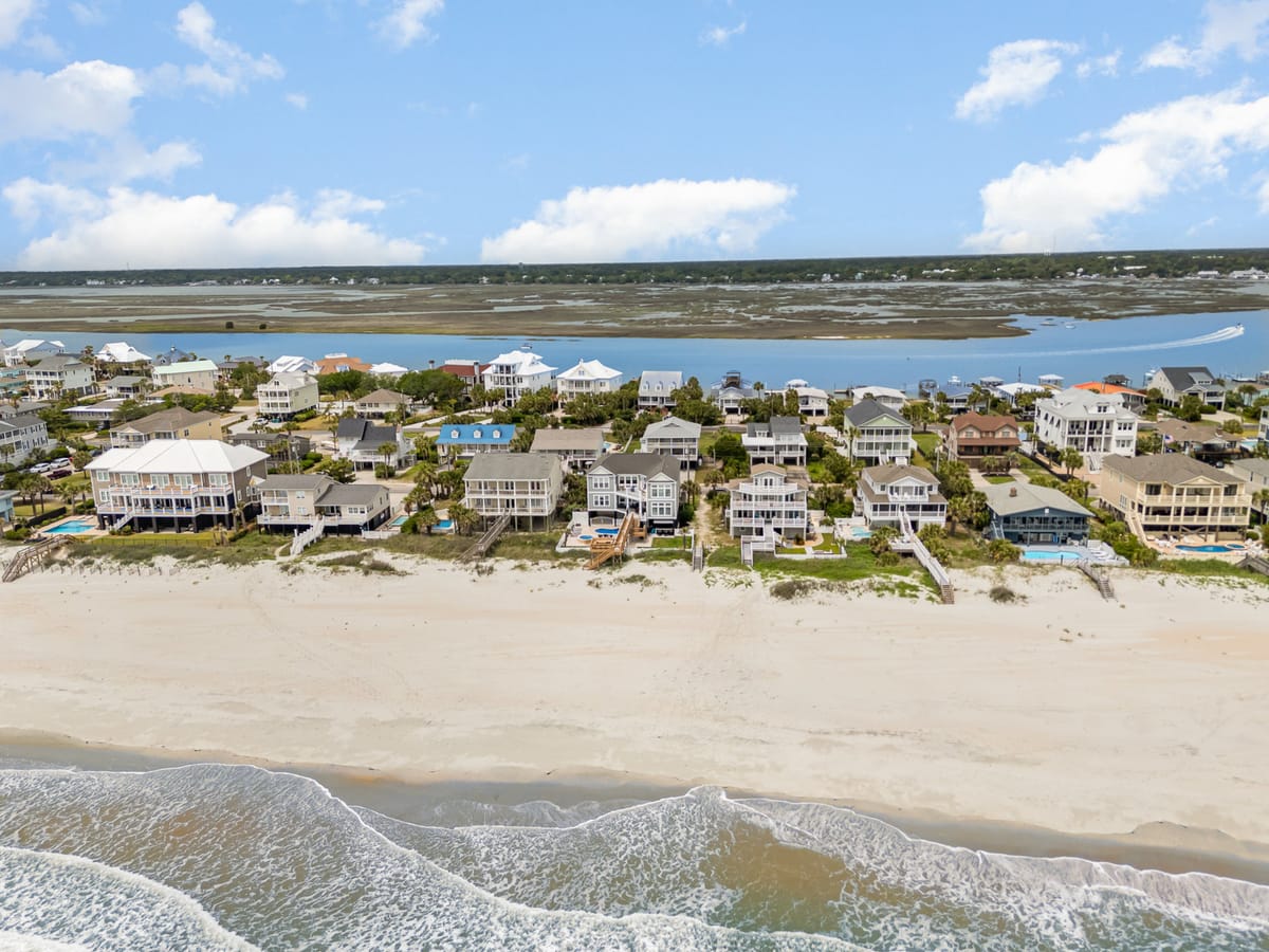Aerial View of Coastal Beachfront Homes with Private Access and Scenic Waterway Backdrop under Bright Blue Sky and Fluffy Clouds