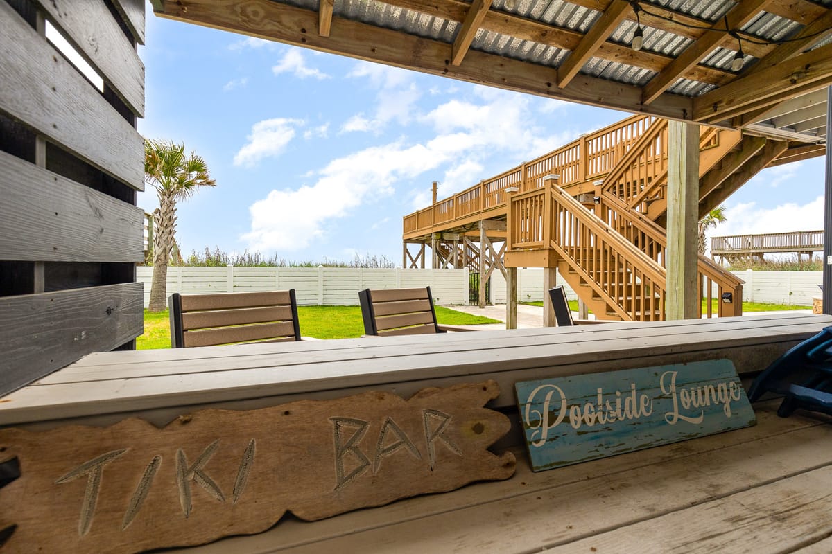 Beachfront Tiki Bar and Poolside Lounge with Wooden Deck and Staircase Under a Clear Blue Sky