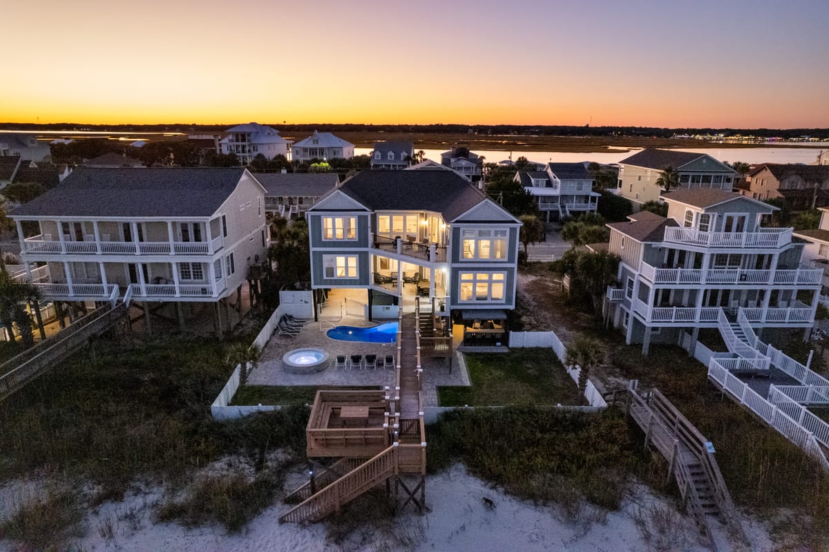 Luxurious Coastal Beach House at Sunset with Illuminated Windows, Private Pool, and Elevated Boardwalk Amidst Seaside Neighborhood