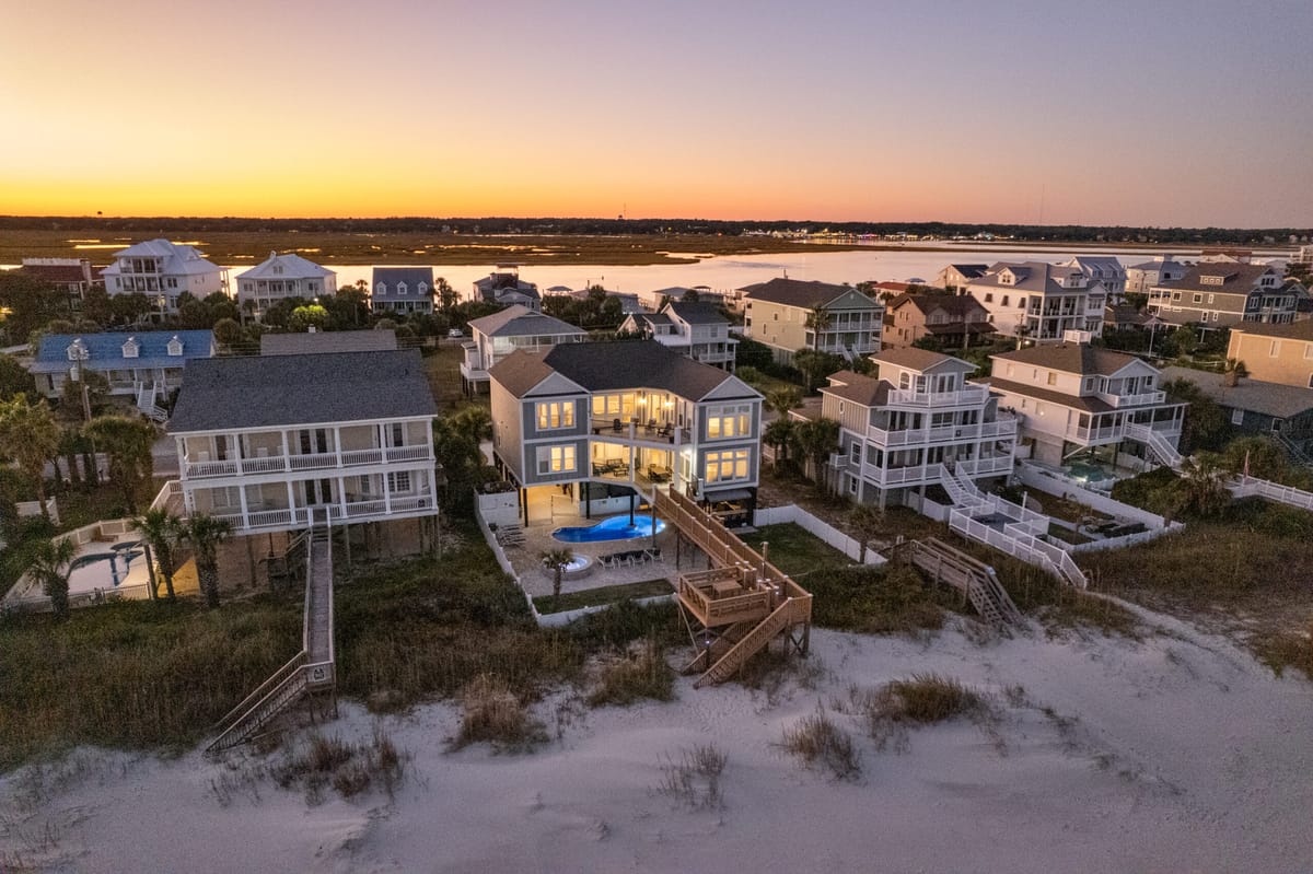 Coastal Beachfront Houses at Sunset with Illuminated Interiors and Pool Overlooking Calm Waters and Sandy Shoreline