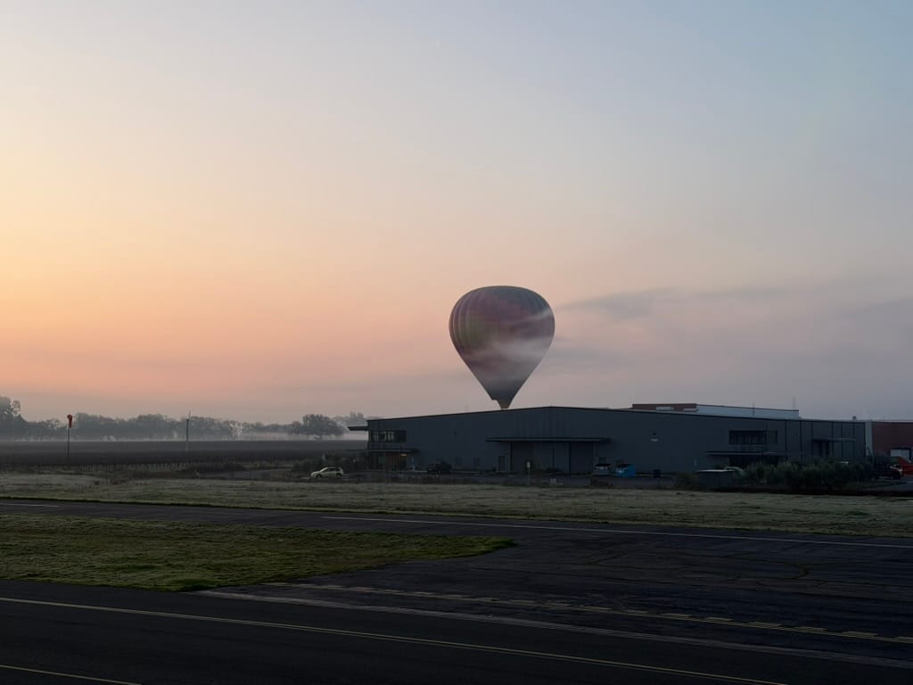 Vibrant Hot Air Balloon Ascending Over Industrial Building at Peaceful Sunrise with Misty Horizon