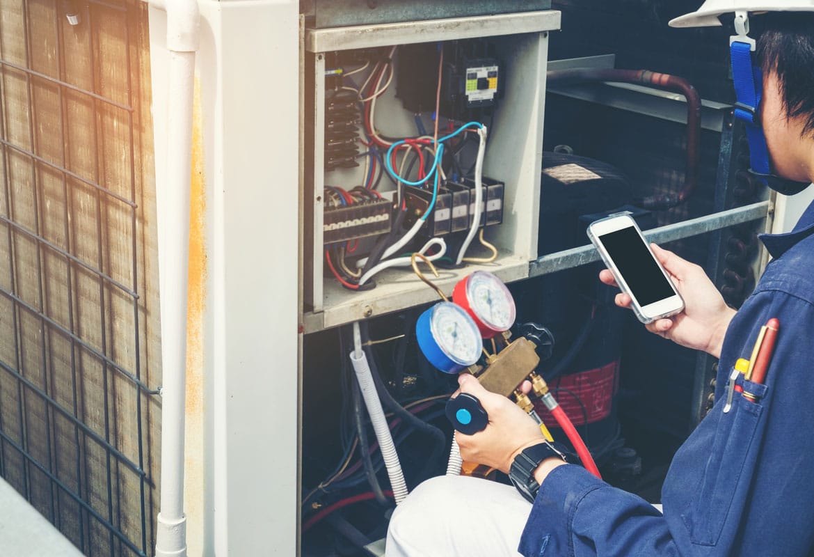HVAC Technician Diagnosing Air Conditioning Unit with Smartphone and Pressure Gauges in Hand