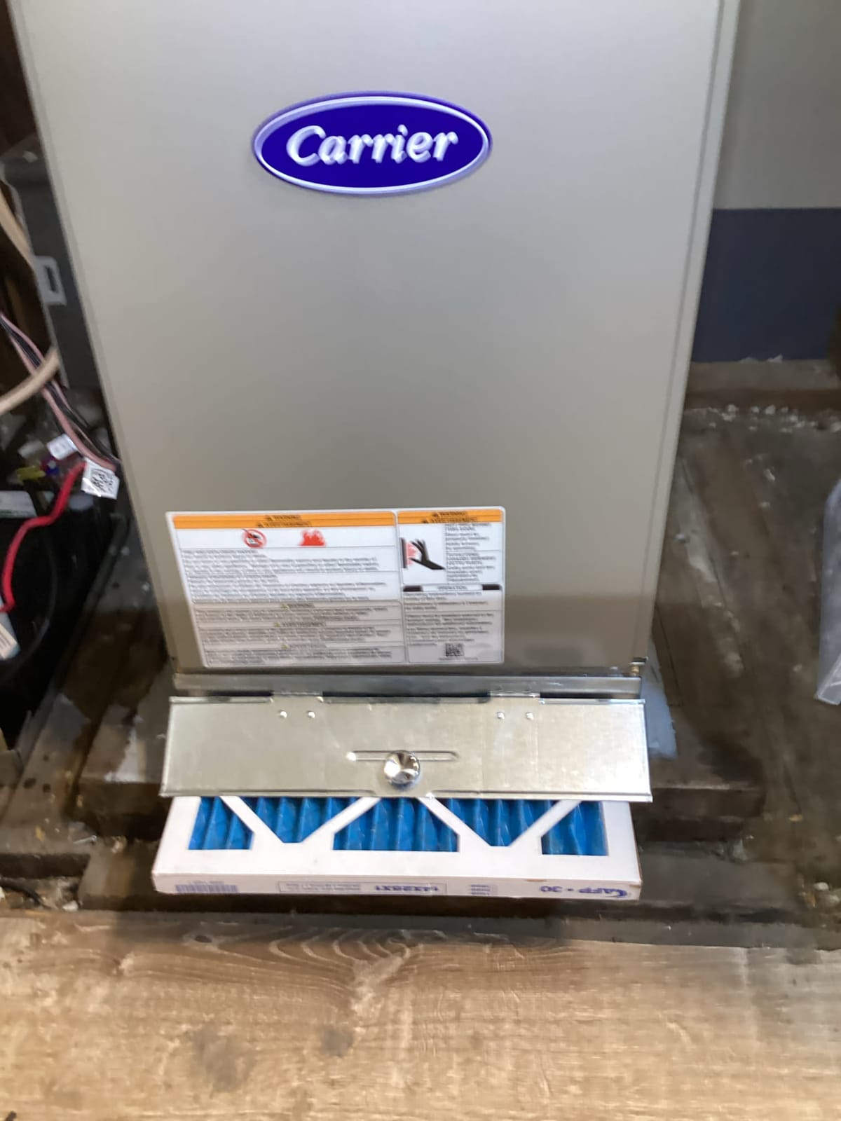 Carrier HVAC Unit with Open Filter Compartment Showing Blue Air Filter on Wooden Floor Surface