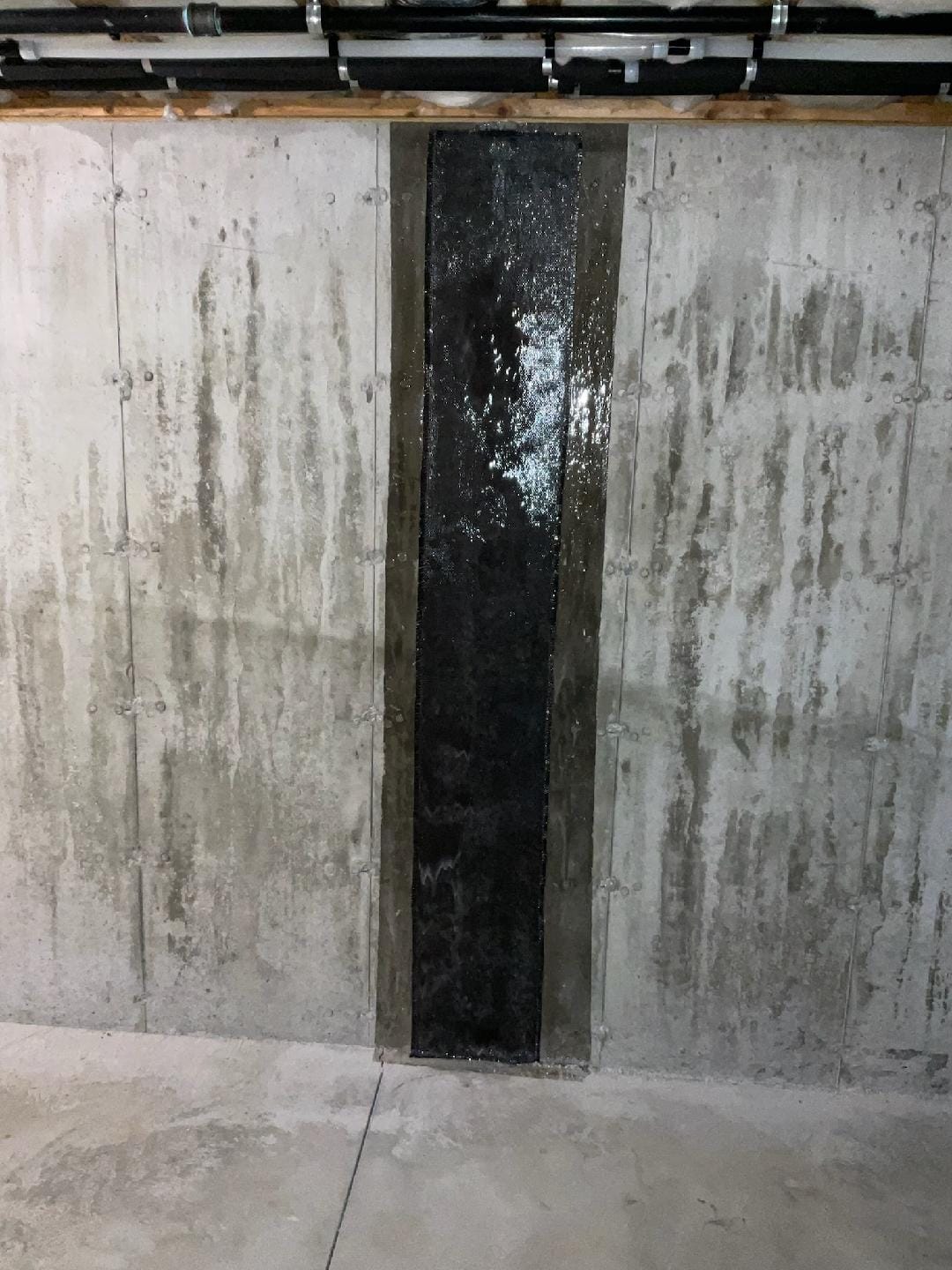 Vertical Carbon Fiber Reinforcement Strip on Concrete Wall with Exposed Pipes Overhead in Industrial Setting