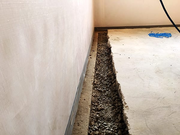 Concrete Floor with Exposed Trench along Wall Revealing Gravel Base and Blue Construction Material in Corner