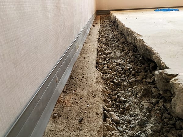 Exposed Foundation with Gravel and Uneven Edge Next to Wall in Construction Area