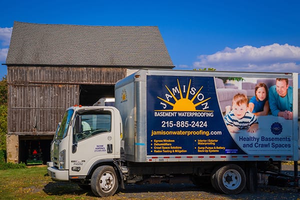 Delivery Truck for Basement Waterproofing Service Parked in Front of Rustic Barn with Clear Blue Sky