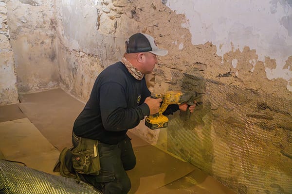Worker Installing Waterproof Membrane on Crumbling Basement Wall Using Power Drill for Renovation and Structural Reinforcement